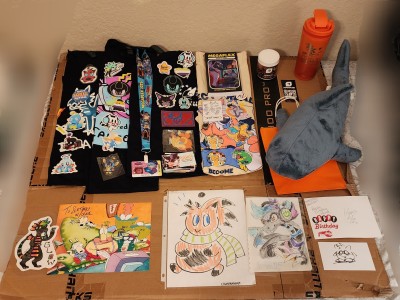 Photo of a majority of merchandise purchased at Megaplex 2025 Dealer's Den and Artist Alley. Some items may include raffle prizes and a badge of Sertimus' own.
